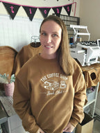 Woman wearing a brown sweatshirt with 'The Coffee Shop Book Club' design in a casual setting.