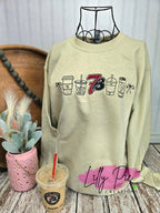 Beige sweatshirt with coffee cup graphics on a wooden surface with a plant and cup.