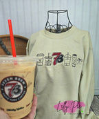 Light green sweatshirt with 'Seven Brew' and coffee cup graphics, held next to a Seven Brew coffee cup.
