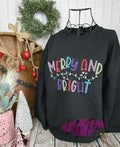 Black sweatshirt with 'Merry and Bright' text in colorful lights, displayed on a stand with Christmas decorations.