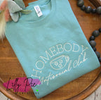 Teal sweatshirt with 'Homebody Antisocial Club' text and a cup graphic on a wooden surface, featuring the brand 'Lilly Pie Creations'.