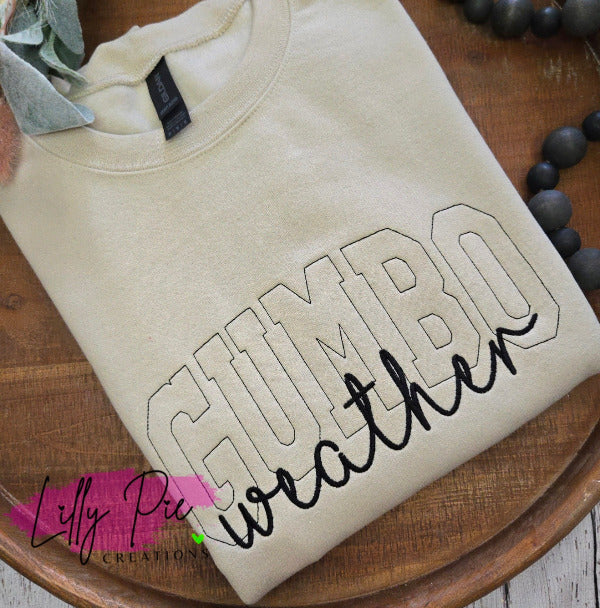 Beige sweatshirt with 'Gumbo weather' text on a wooden surface, featuring Lilly Pie Creations logo.