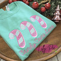 Folded teal shirt with candy cane design and text on a wooden surface with Christmas decorations.