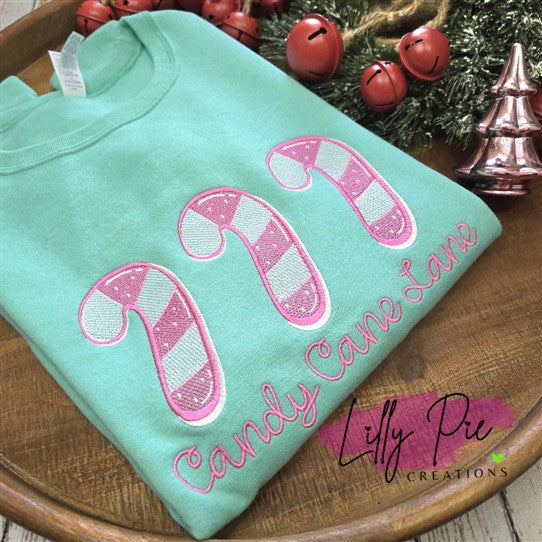 Folded teal shirt with candy cane design and text on a wooden surface with Christmas decorations.