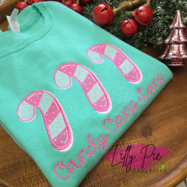 Mint green shirt with candy cane design and 'Candy Cane Lane' text on a wooden surface with Christmas decorations.