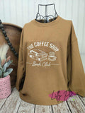 Brown sweatshirt with 'The Coffee Shop Book Club' design on a wooden surface.